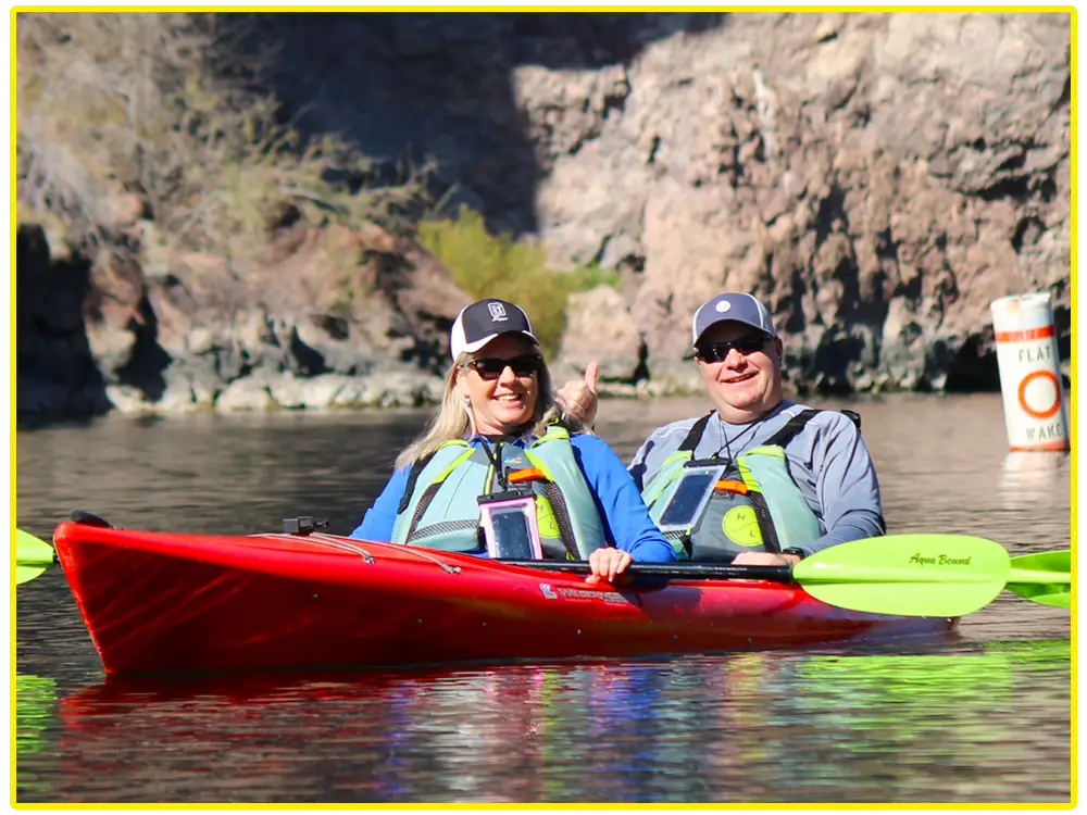 Smiling couple kayaking in a tandem red kayak on the Colorado River near Emerald Cave.