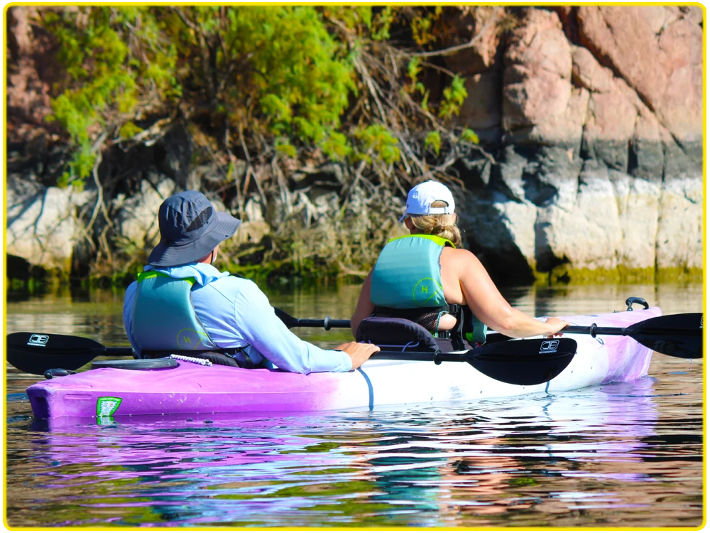 Two kayakers in a purple tandem kayak navigating the Colorado River near Hoover Dam and Black Canyon, ideal for couples, scenic kayaking tours, unique outdoor activities, and paddle adventures in rugged desert landscapes and canyon walls.