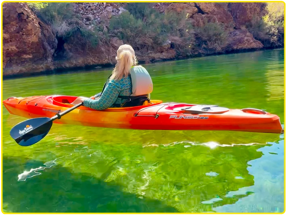 Woman paddling an orange kayak through the stunning green waters of Emerald Cove, surrounded by desert cliffs and tranquil nature.