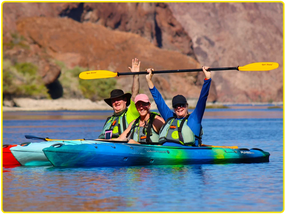 Three kayakers celebrating their kayaking adventure on the Colorado River, surrounded by stunning desert cliffs, ideal for group kayaking, family-friendly outdoor activities, scenic tours, and celebrating fun moments on the water.