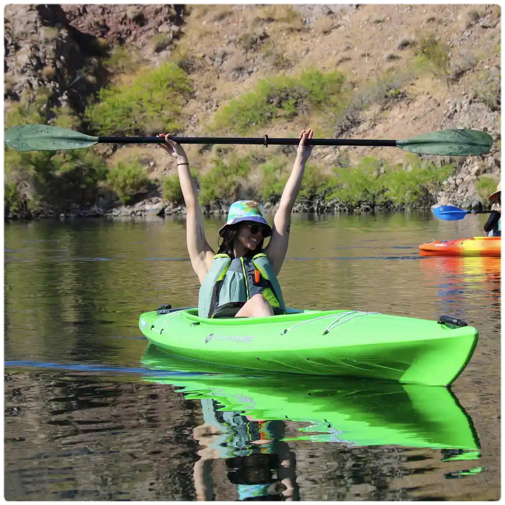 Excited kayaker raising her paddle in a bright green kayak during a beginner-friendly guided tour to Emerald Cove on the scenic Colorado River.