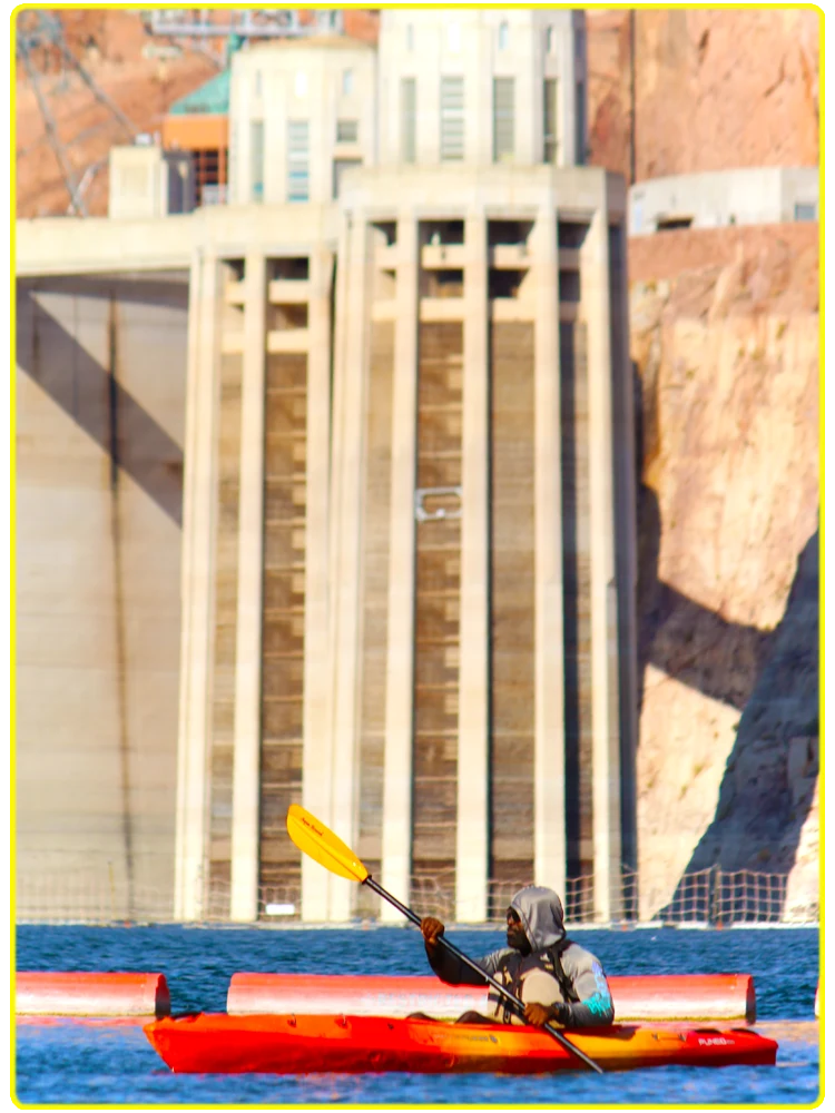 Top 10 FAQs. A kayaker paddling in a red kayak near the iconic Hoover Dam with clear blue waters and stunning canyon walls in the background.