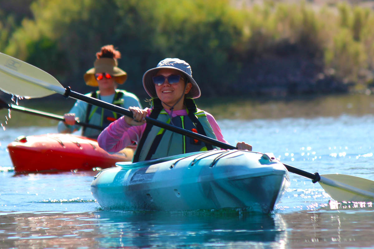 Group of kayakers paddling on the Colorado River, enjoying an outdoor adventure with scenic cliffs in the background.