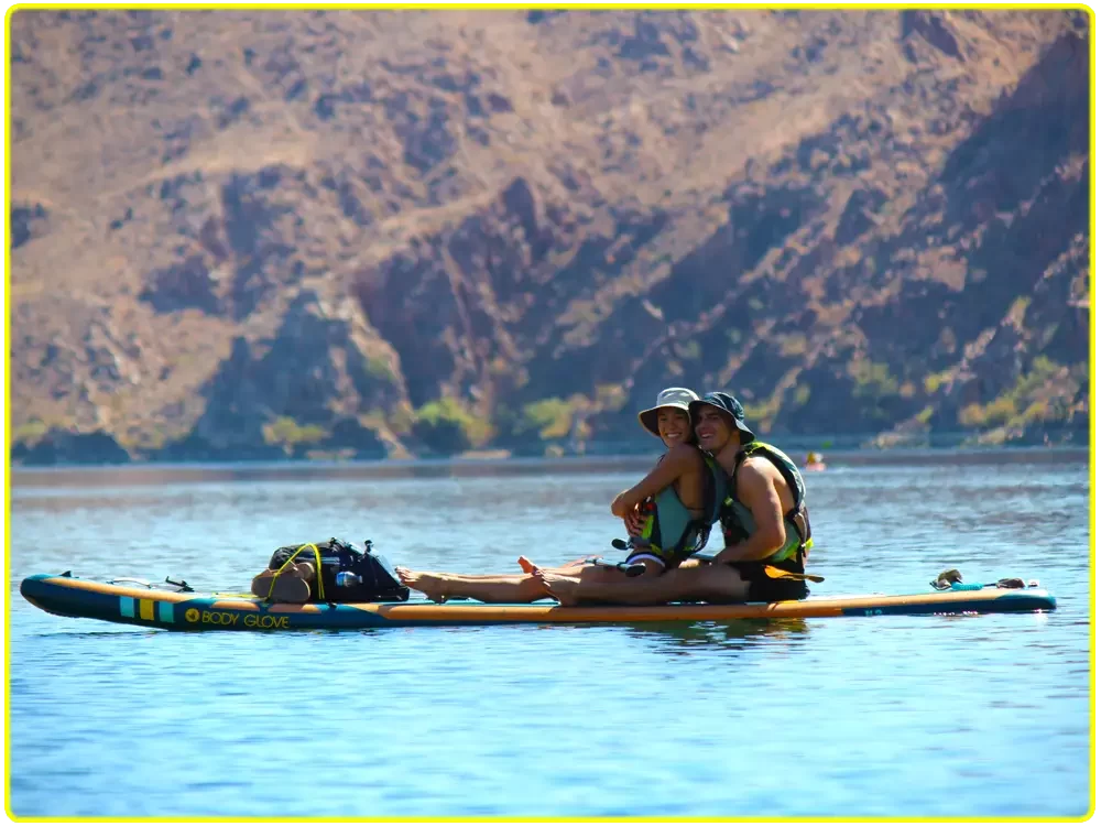 Couple enjoying a guided stand-up paddleboard adventure on the Colorado River near Emerald Cove, with calm, crystal-clear waters, breathtaking canyon views, and a beginner-friendly paddleboarding experience close to Willow Beach and Black Canyon.